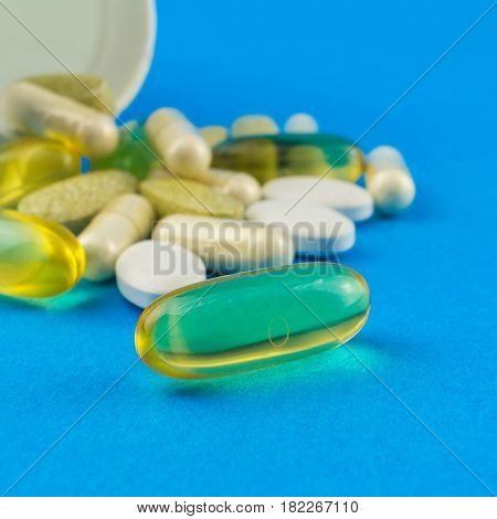 Supplement of omega-3 capsule on foreground in the focus vitamin complex glucosamine capsules and white container on blue background.