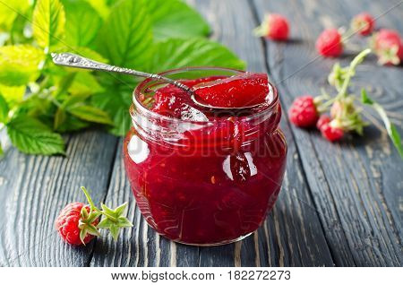 Raspberry jam and fresh raspberries on a wooden table in the garden