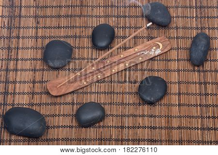 Hand carved burner, holder with sandalwood incense and polished black river pebbles on bamboo placemat