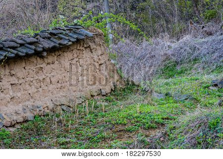 Mud brick wall with black tile roof fallen into state of disrepair in wooded area South Korea