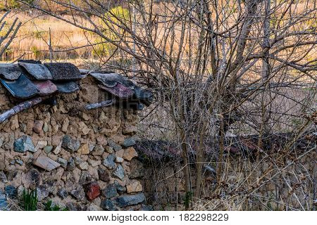 Mud brick wall with black tile roof fallen into state of disrepair in wooded area South Korea