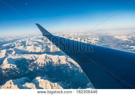 Looking through the window aircraft during flight a snow covered Italian and Osterreich Alps with blue sky without clouds.
