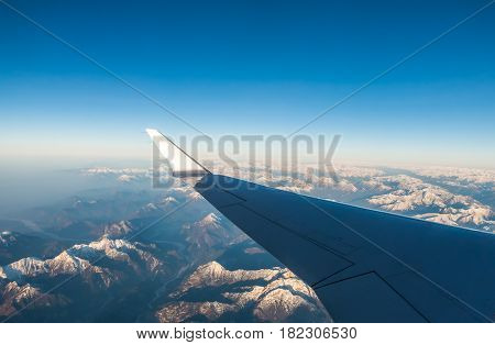 Looking through the window aircraft during flight a snow covered Italian and Osterreich Alps with blue sky without clouds.