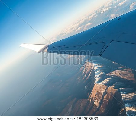 Looking through the window aircraft during flight a snow covered Italian and Osterreich Alps with blue sky without clouds.