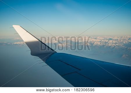 Looking through the window aircraft during flight a snow covered Italian and Osterreich Alps with blue sky without clouds.