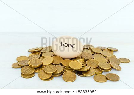 An egg with the inscription `home` lies on coins on a white background