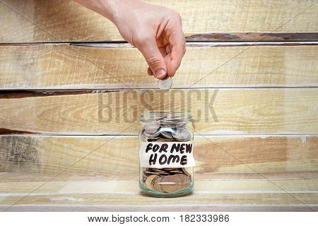 The hand puts a coin in a glass jar with the inscription 