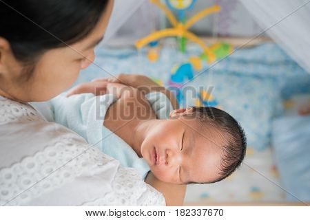 Mother takecare asian new born baby to sleep in thr cradle