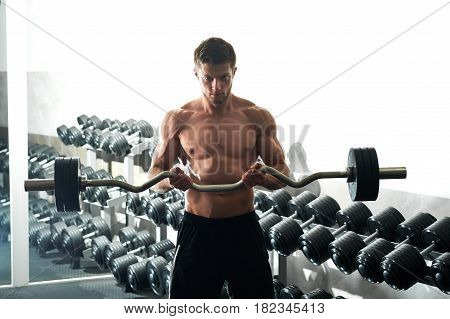 Horizontal shot of a shirtless muscular athletic young man doing biceps curls exercising with EZ curl bar at the gym workout fitness toning bodybuilding muscles sport activity concept.