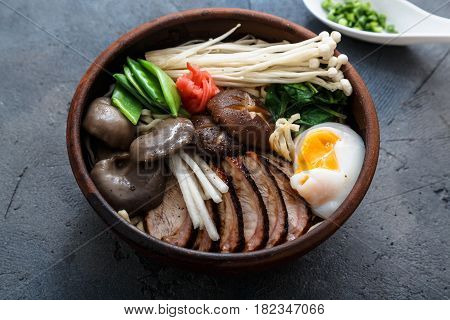 Ramen noodles bowl with egg, enoki, shiitake mushrooms, duck and onion, dark background, close view