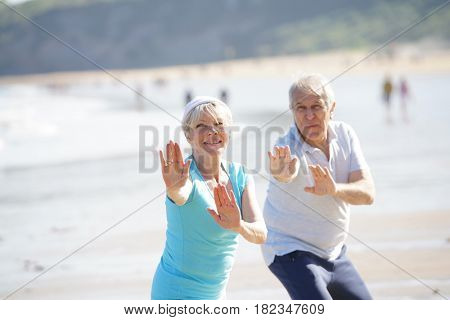 Senior couple doing stretching exercices on the beach