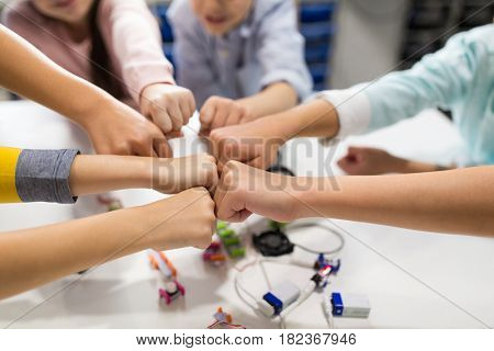 education, children, technology, science and people concept - group of happy kids with building kit making fist bump at robotics school