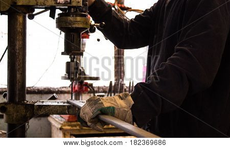 Construction worker drills hole in rod of metal iron using industrial drill in a bright workshop / workshed / factory