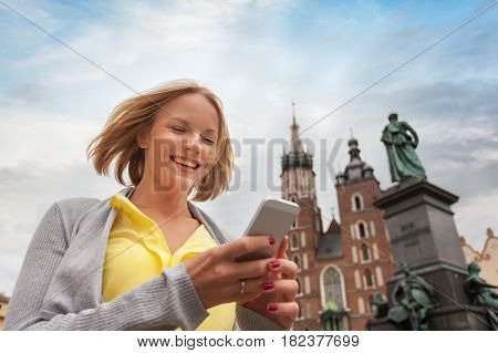Female tourist in a yellow dress stands on a background of the church of St. Mary in Krakow with a phone. Basilica Mariacka. Krakow. Poland.
