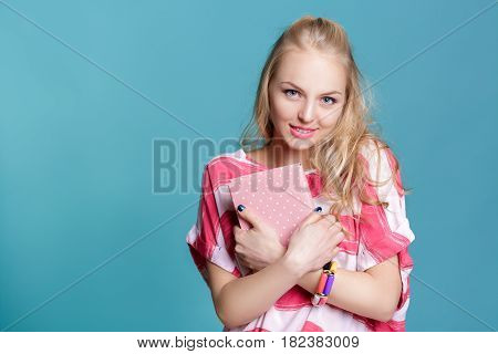young attractive blond woman holding a pink book on blue background