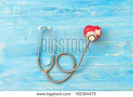 One single alone red heart love shape hand exercise ball with bandage MD medical doctor physician's stethoscope blue wood background