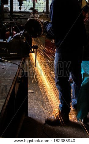 Craftsman uses angle grinder to cut piece of wrought iron metal with sparks flying and protective industrial gloves in workshop