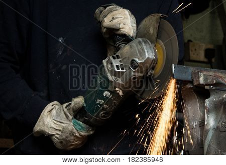 Craftsman uses angle grinder to cut piece of wrought iron metal with sparks flying and protective industrial gloves