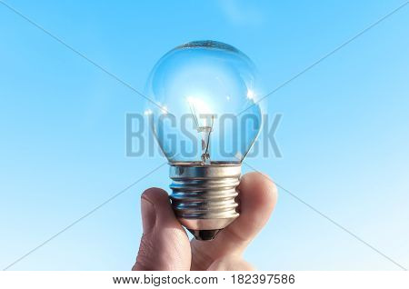 Concept idea of a burning incandescent lamp in a hand against a clear blue sky background from solar energy power