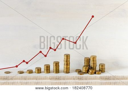 Golden coins stacks arranged as a graph with red arrow on a wooden background. Business growth and Saving money concept