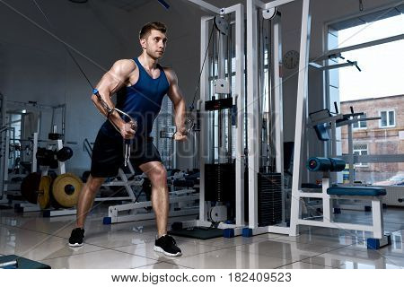 Athletic man in a T-shirt standing training on a exercise machine in the gym