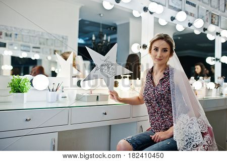 Young Girl Bride Sitting On Chair Near Mirror At Beauty Salon And Holding Star With Sign: Happy Girl