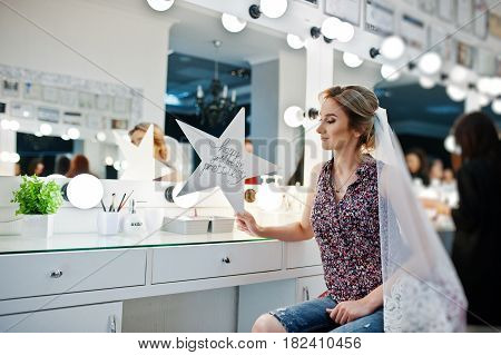 Young Girl Bride Sitting On Chair Near Mirror At Beauty Salon And Holding Star With Sign: Happy Girl