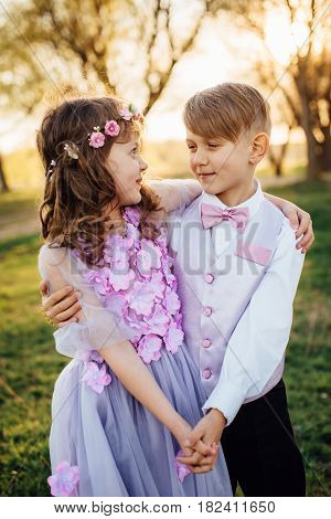 Girl and boy in smart clothes walking in spring park at sunset