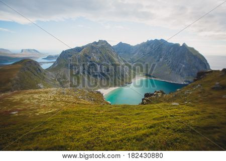 Beautiful Vibrant Norwegian Mountain Landscape from Ryten peak - famous mountain in Lofoten Islands, Moskenes municipality, Nordland with a view of Kvalvika beach, with hiking tourists and blue sky
