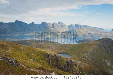 Beautiful Vibrant Norwegian Mountain Landscape from Ryten peak - famous mountain in Lofoten Islands, Moskenes municipality, Nordland with a view of Kvalvika beach, with hiking tourists and blue sky