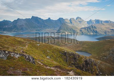 Beautiful Vibrant Norwegian Mountain Landscape from Ryten peak - famous mountain in Lofoten Islands, Moskenes municipality, Nordland with a view of Kvalvika beach, with hiking tourists and blue sky