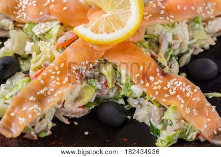 Salad with salmon vegetables lemon and black olives on black plate. Close up image.