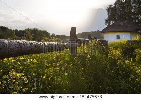 Ukrainian village. Wooden fence. Wattle and daub house under the thatched roof in the background. Rural landscape before the rain.