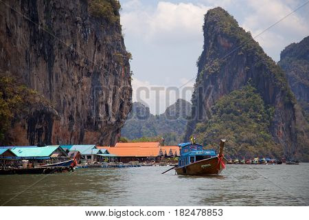 Muslim floating village of Panyi, Thailand, with colorful fishing boats and dramatic cliffs in background.