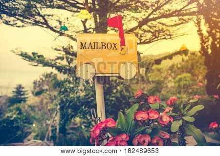 Old yellow stained metal mailbox has red flag raised up to indicate mail has arrived. Outdoor on summer day with bright sunlight at sunset. Vintage effect tone.
