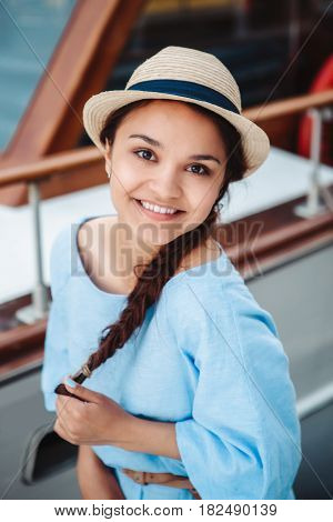 Portrait of beautiful smiling white Caucasian brunette girl on boat yacht pier quay in blue dress and straw hat posing making funny emotional faces expressions having fun