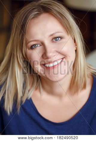 Closeup portrait of beautiful smiling young middle age Caucasian woman in blue shirt looking in camera with long blonde hair bob and blue eyes flirty look