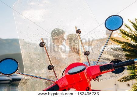 A red retro moped parked at the marina. In Budva, Montenegro. Silhouette of a kissing couple through a glass with raindrops.