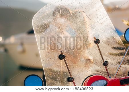 A red retro moped parked at the marina. In Budva, Montenegro. Silhouette of a kissing couple through a glass with raindrops.