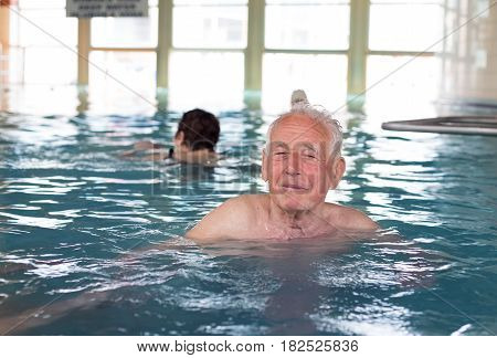 Senior man swimming in indoor pool and enjoying hydrotherapy