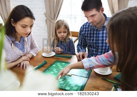Happy young family plaing board game with two daughters