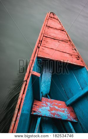 The front of a colourful wooden canoe cuts through the still water of Phewa (Fewa) Lake in Pokhara Nepal.