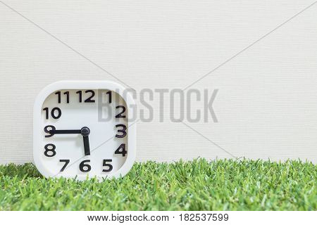Closeup white clock for decorate show a quarter to six o'clock or 5:45 p.m. on green artificial grass floor and cream wallpaper textured background with copy space