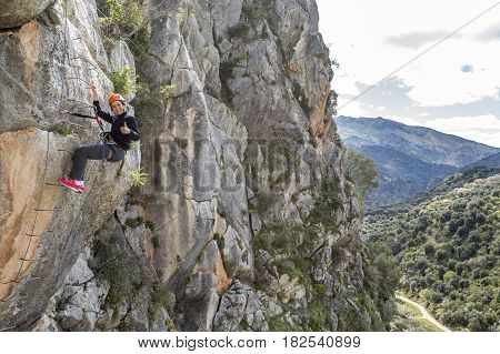 Woman climbing up to the mountain gesturing thumb up and looking at camera