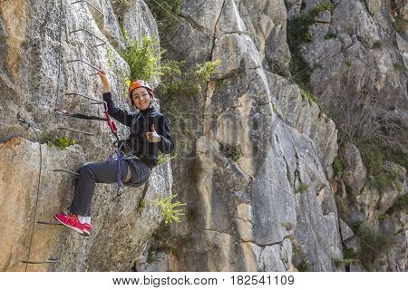 Woman climbing up to the mountain gesturing thumb up and looking at camera