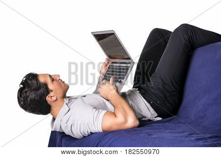 Young attractive man working with computer while laying in awkward position on couch, on white background