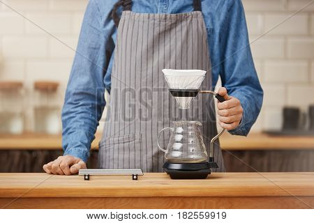 Closeup portrait of nice barista in apron at bar counter about to make pourover coffee.