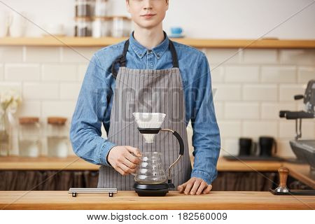 Cropped image of nice barista in apron at bar counter about to make pourover coffee.