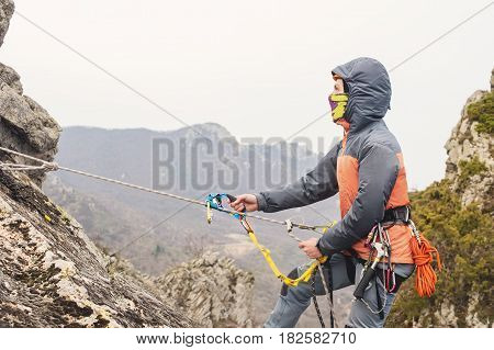 The Young Man climbs the rock on a rope with safety belts, insurance and rope, in full mountaineering equipment and a helmet and hood