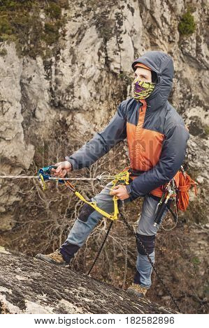 The Young Man climbs the rock on a rope with safety belts, insurance and rope, in full mountaineering equipment and a helmet and hood